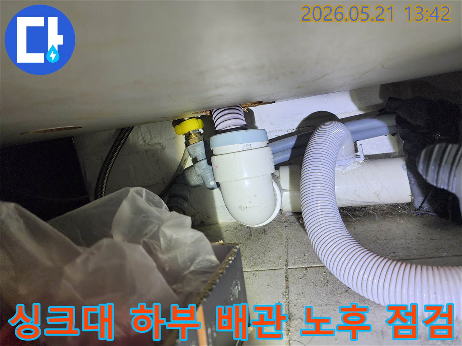 싱크대 하부의 오래된 배수관과 급수관의-노후 상태를 면밀히 점검하는 현장 사진입니다.