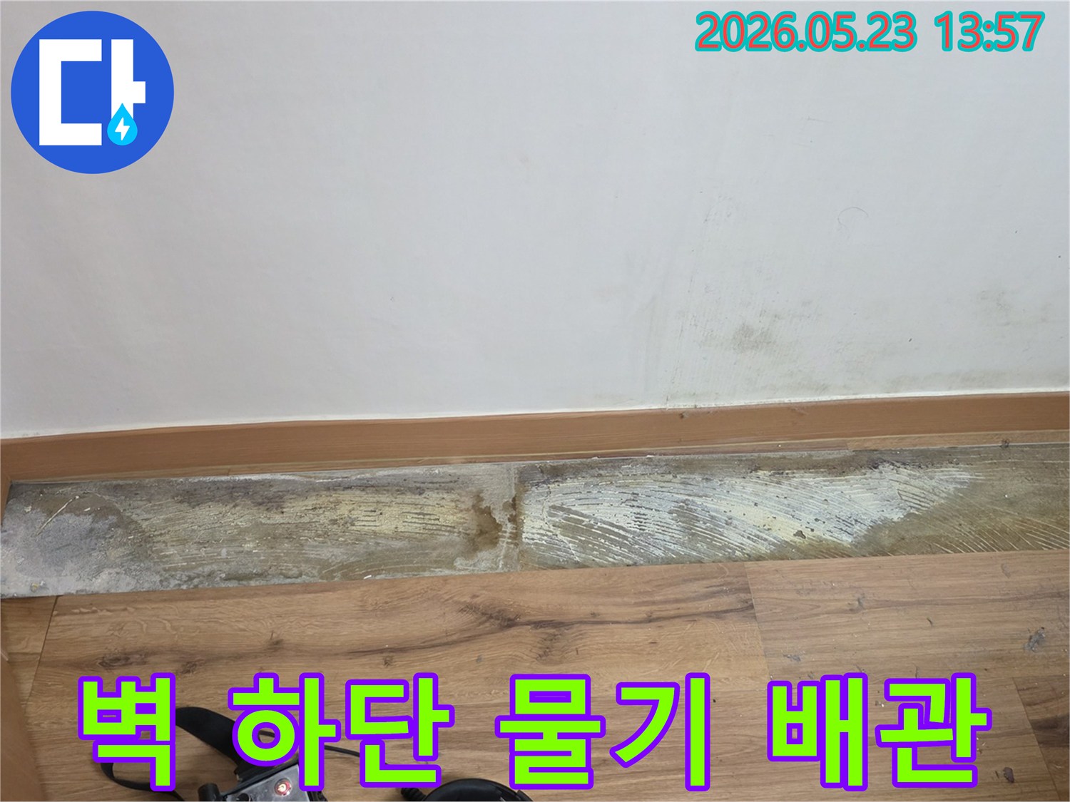 누수 탐지 장비가-바닥에 놓인 채-벽 하단에-발생한-물기와-곰팡이 흔적을-보여주는-손상된 벽면의-현장 사진