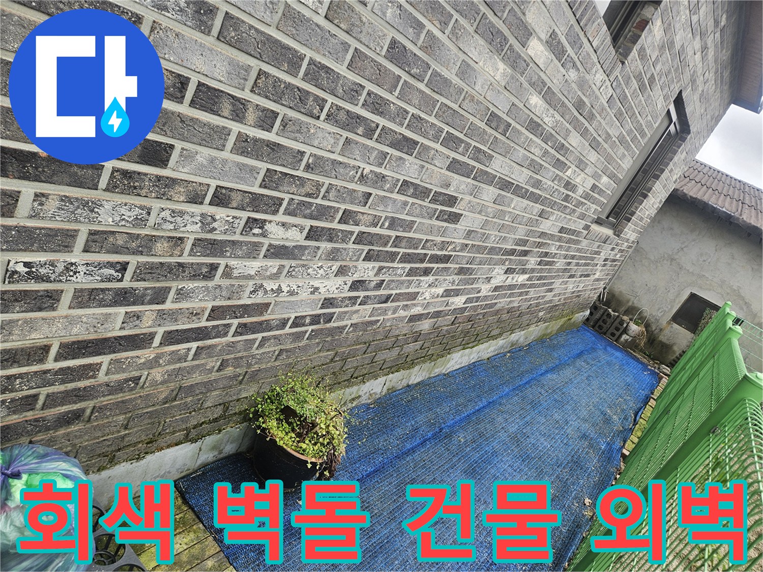 회색 벽돌로 마감된 건물의 외부 벽면과 파란 그물망