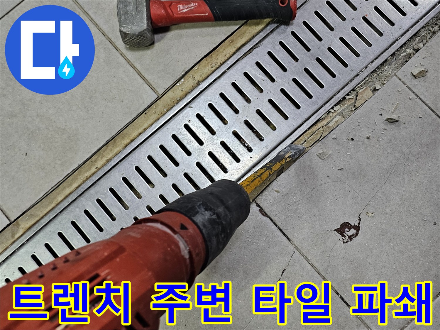 금속 배수로 덮개 옆의 타일을 드릴로 제거하는 현장 사진