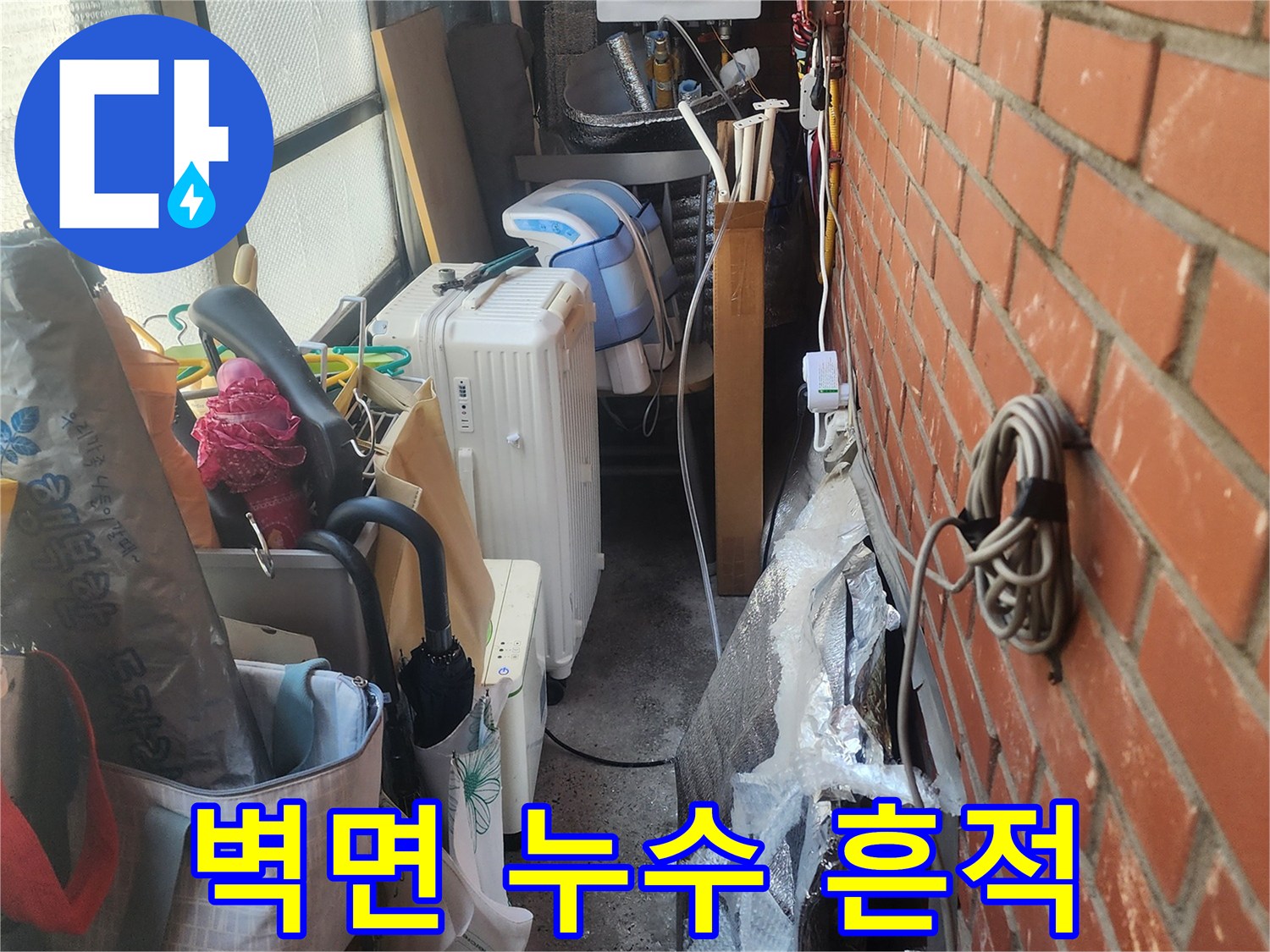 벽돌-벽-아래-복잡하게-얽힌-배관과-생활-용품들-사이에서-발견된-누수-흔적을-보여주는-사진