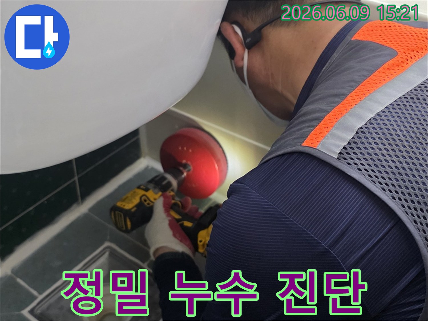 안전-조끼를-입은-엔지니어가-전동-드릴을-사용하여-욕실-배수구-주변을-점검하는-모습
