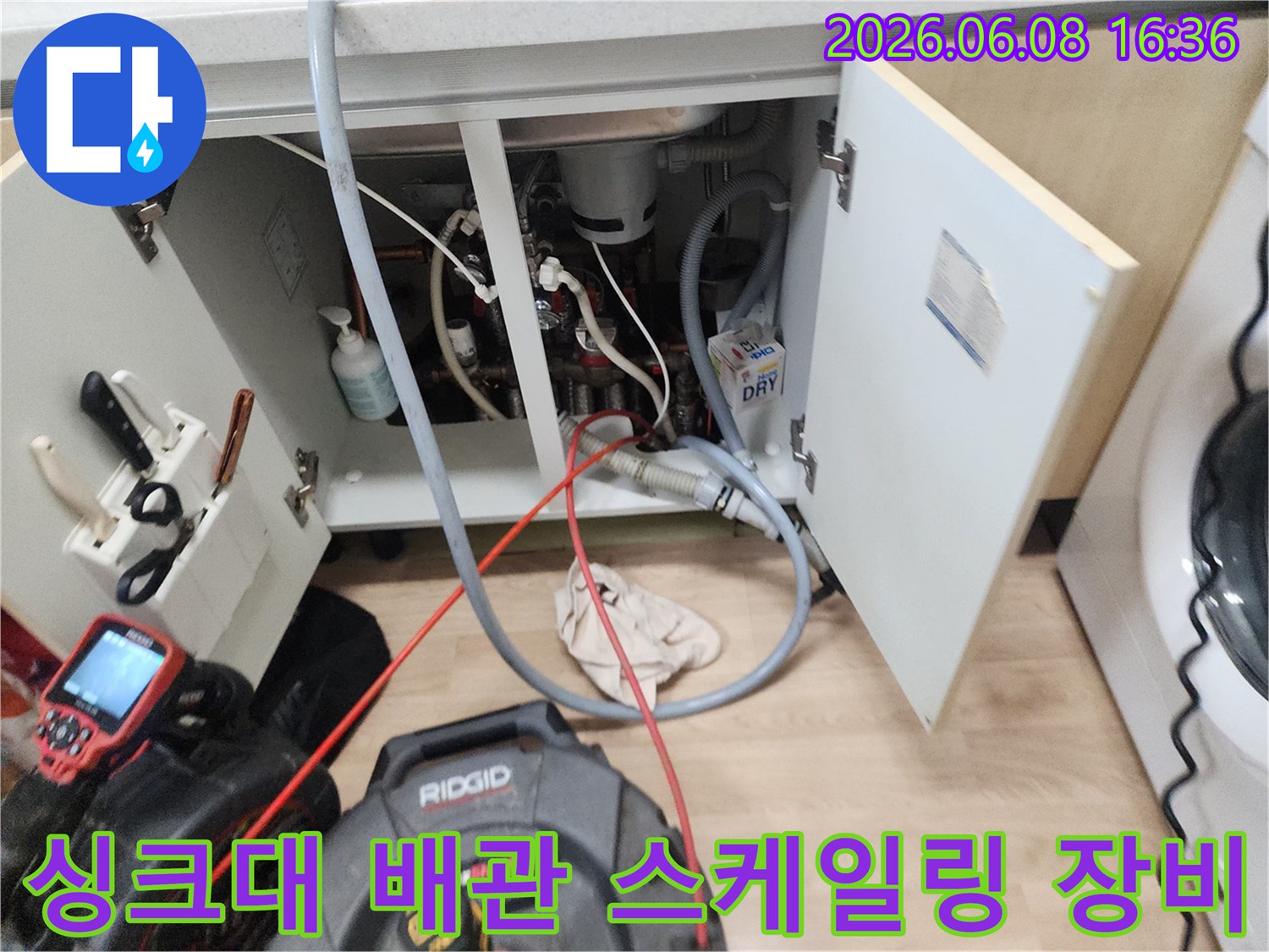 싱크대 하부장 내부의 복잡한 배관과 작업용 붉은색 케이블