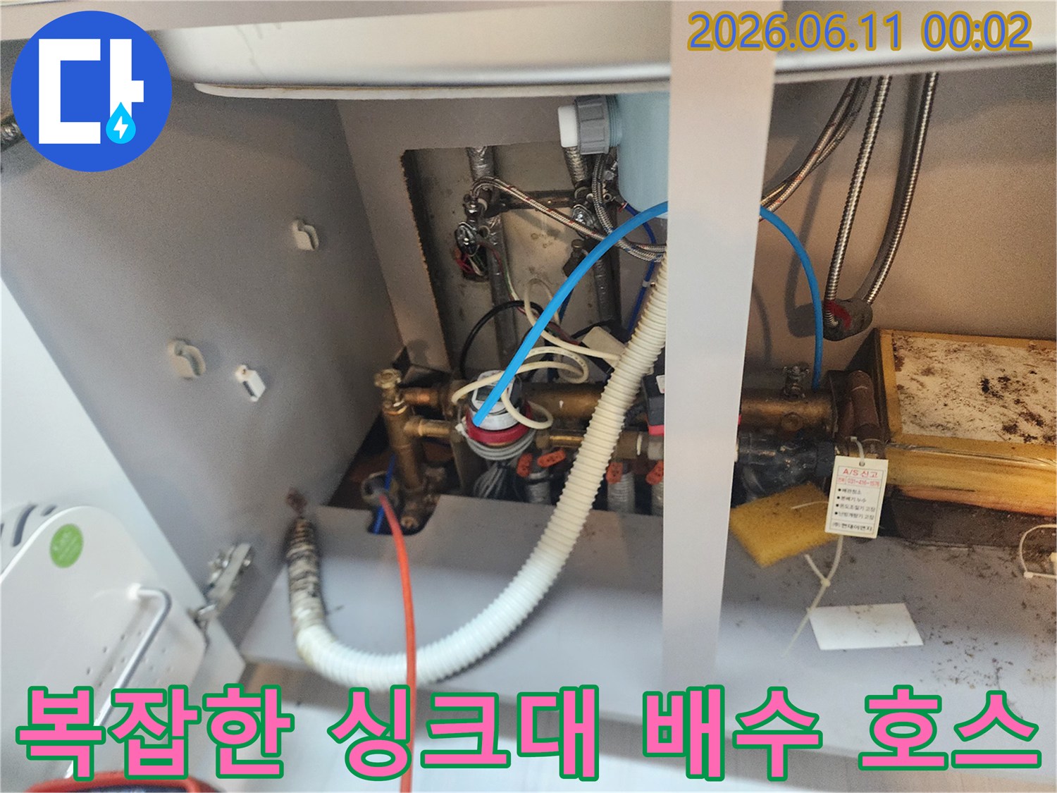 흰색 주름관과 금속 배관이 연결된 싱크대 하부의 작업 모습입니다.