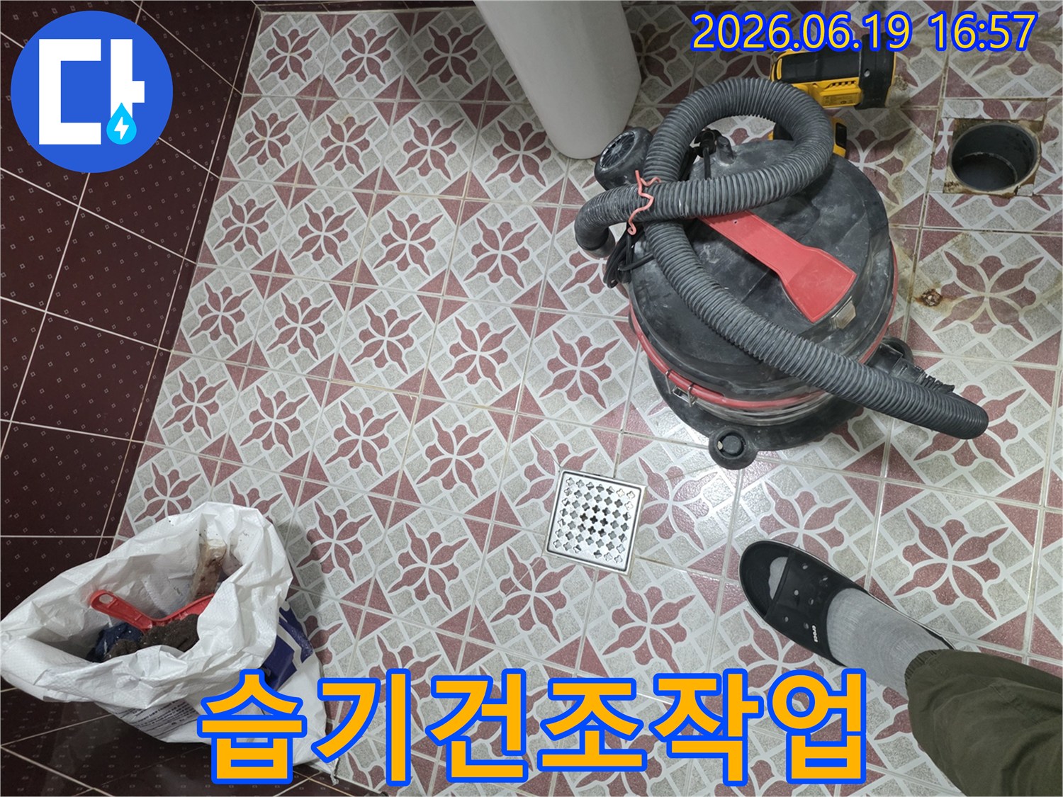화장실 배수구 주변의-누수 처리 과정-습식 청소기로 물을 제거하고-정리된 바닥의 모습-작업자의 발과 함께