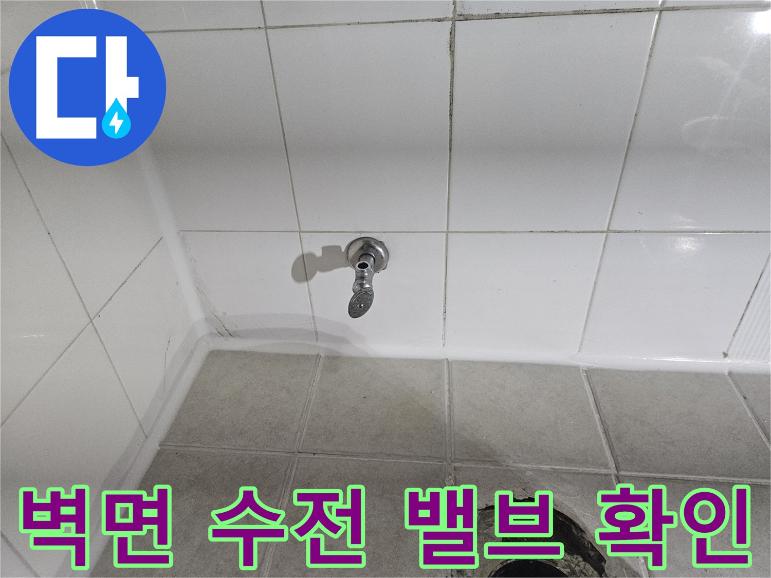 타일 벽면에 설치된 은색 수도 연결 부위입니다.