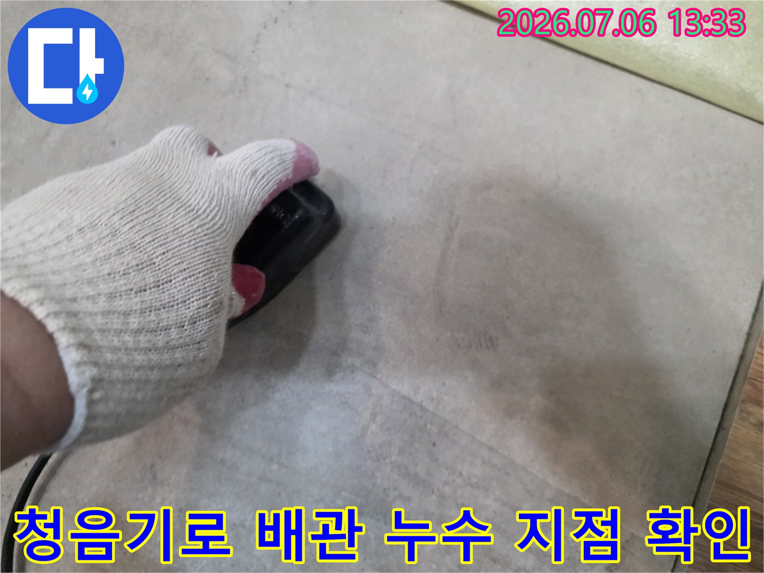 장갑을 낀 손으로 청음기 장비를 사용하여 바닥 아래 매립된 배관의 누수 위치를 정밀하게 찾는 모습