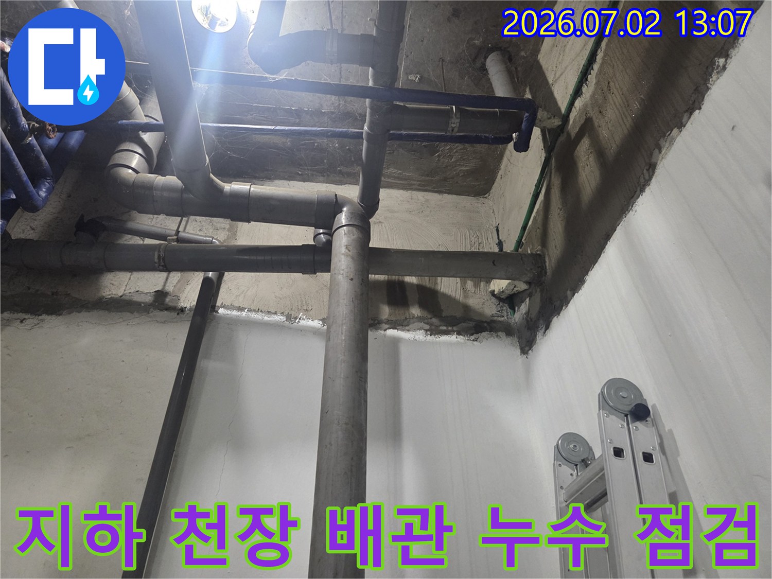 지하 1층 천장에 복잡하게 얽혀 있는 회색과 파란색 하수 배관-벽면의 습기 흔적