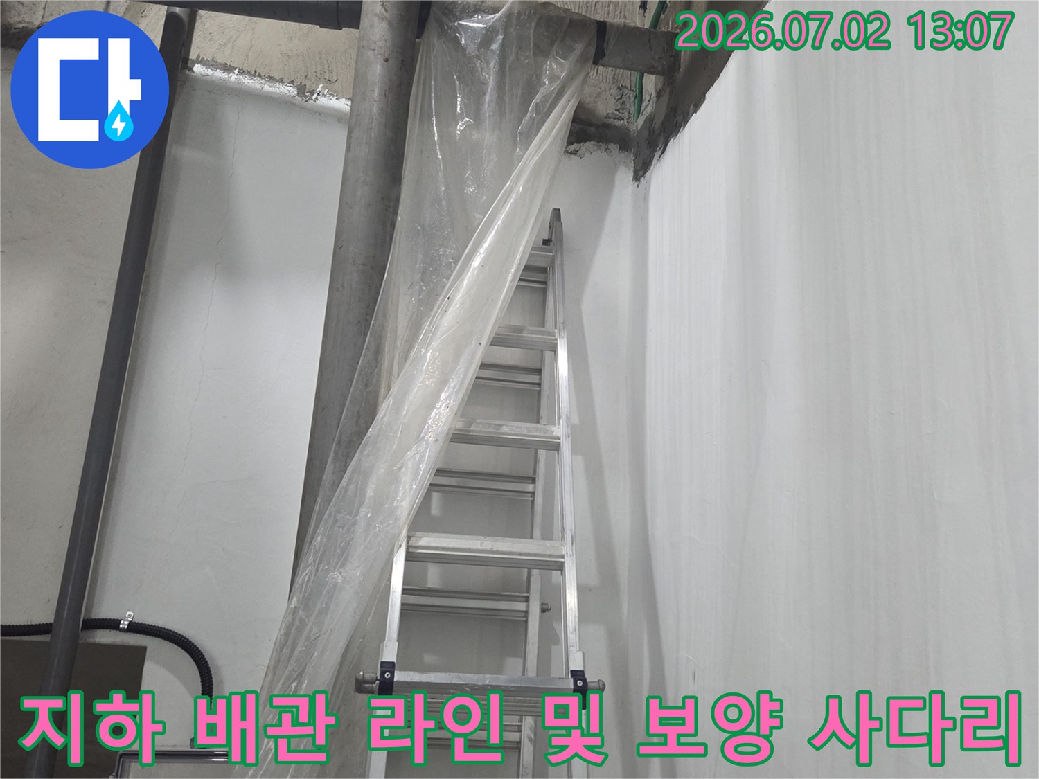 회색 천장 배관 아래로 비닐 커버가 씌워진 알루미늄 사다리가 세워져 있는 모습