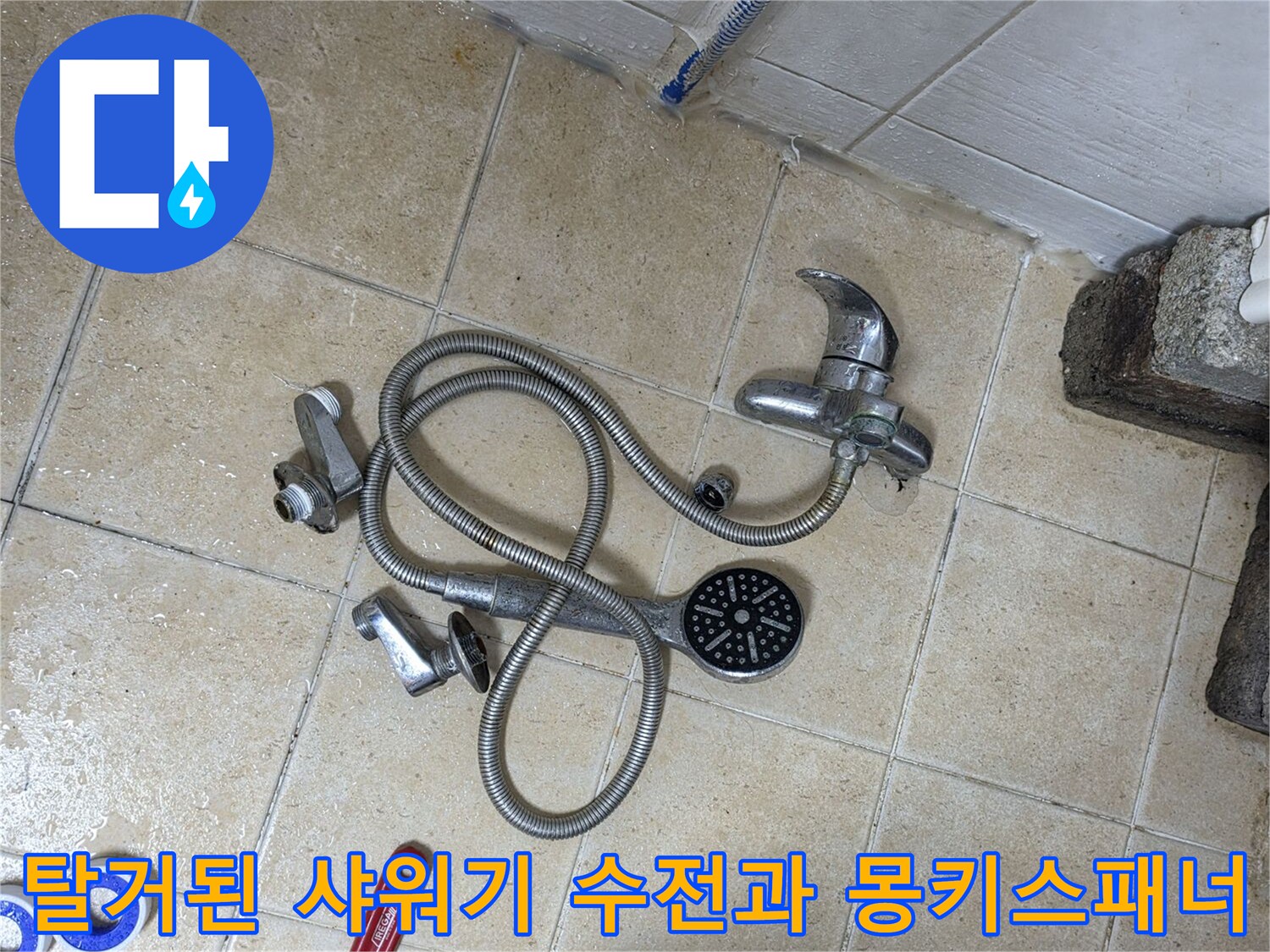 바닥 타일 위에 놓여 있는 탈거된 샤워기 헤드와 몽키스패너