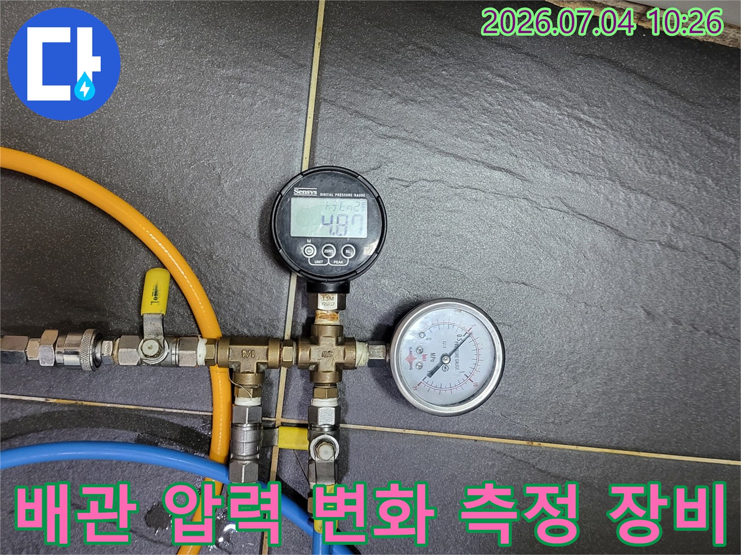 전문가용 디지털 게이지와 노란색 호스를 연결한 배관 점검 장면