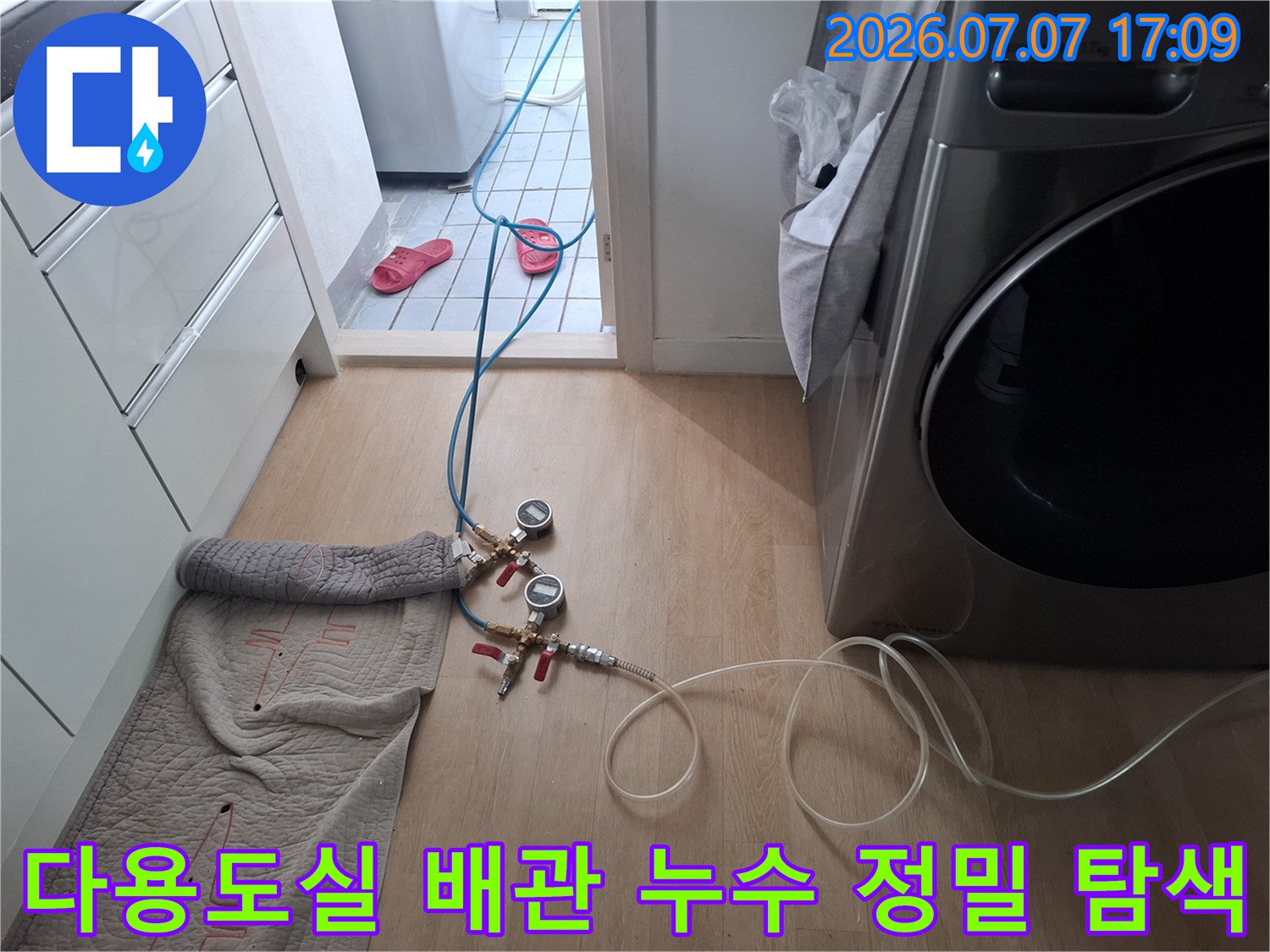 전문 장비와 호스를 연결하여 세탁기 옆 배관 시스템을 점검하는 모습