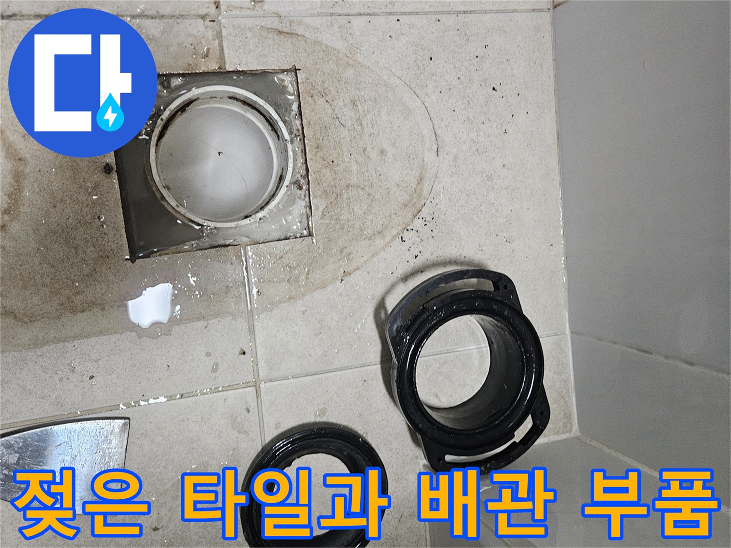 물기에 젖어 어두워진 화장실 바닥 타일과 탈거된 배관 자재