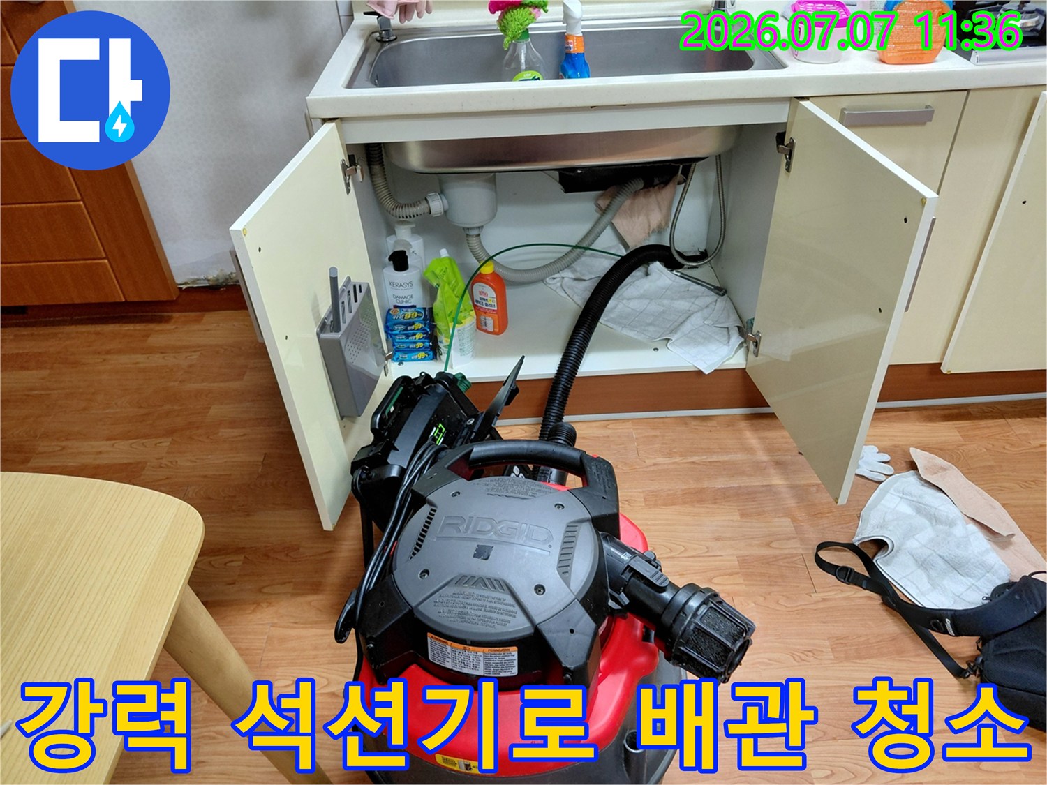 싱크대 하부장의 문을 열고 전문 장비로 배관 내부 오물을 제거하는 모습
