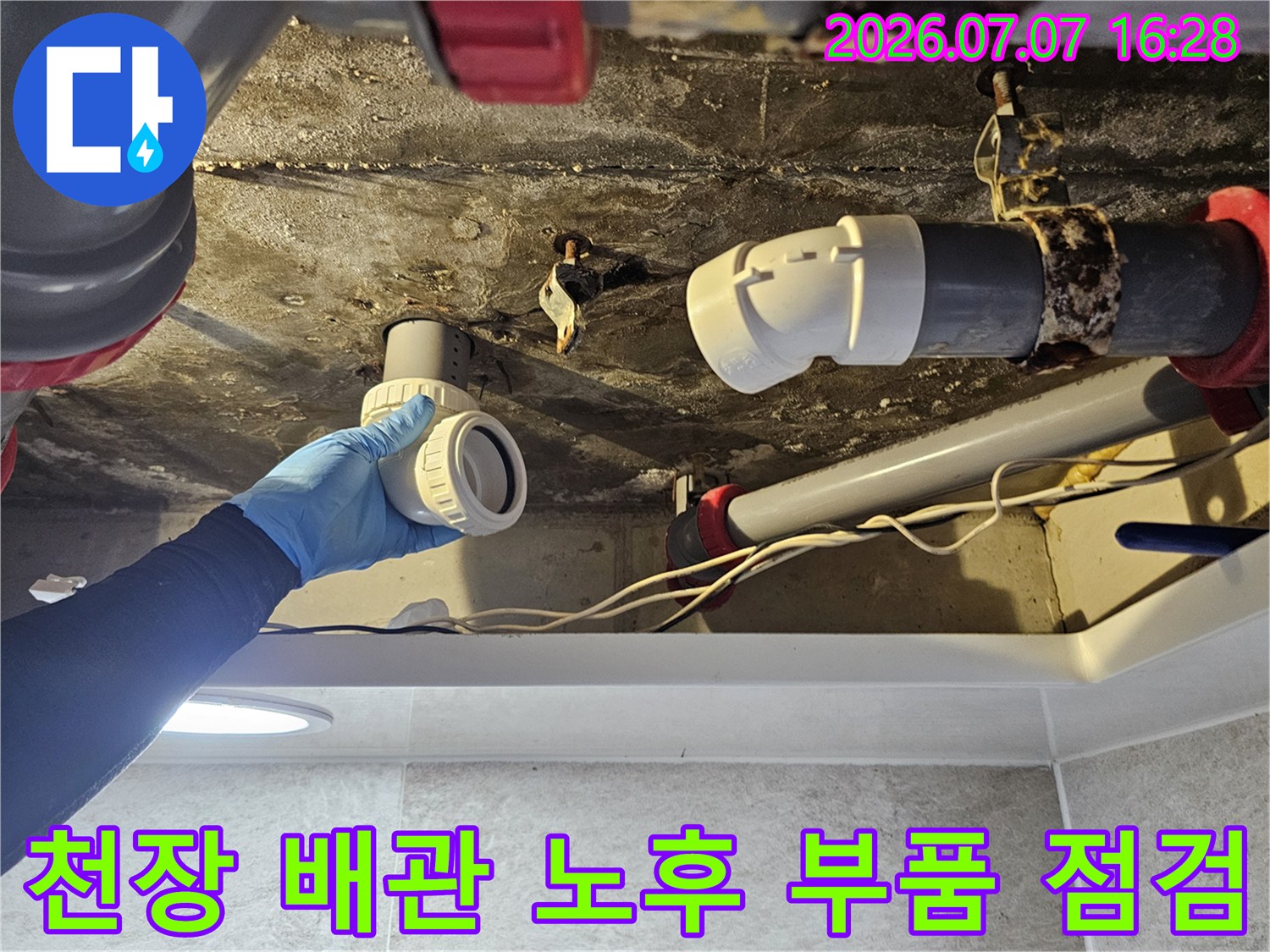 노후된 화장실 천장 배수 배관의 연결 부위를 상세히 점검하는 장면