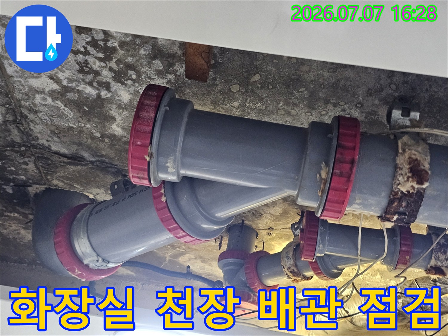 화장실 천장 내부에 노출된 회색 배수 배관과 붉은색 연결 부속을 점검하는 모습