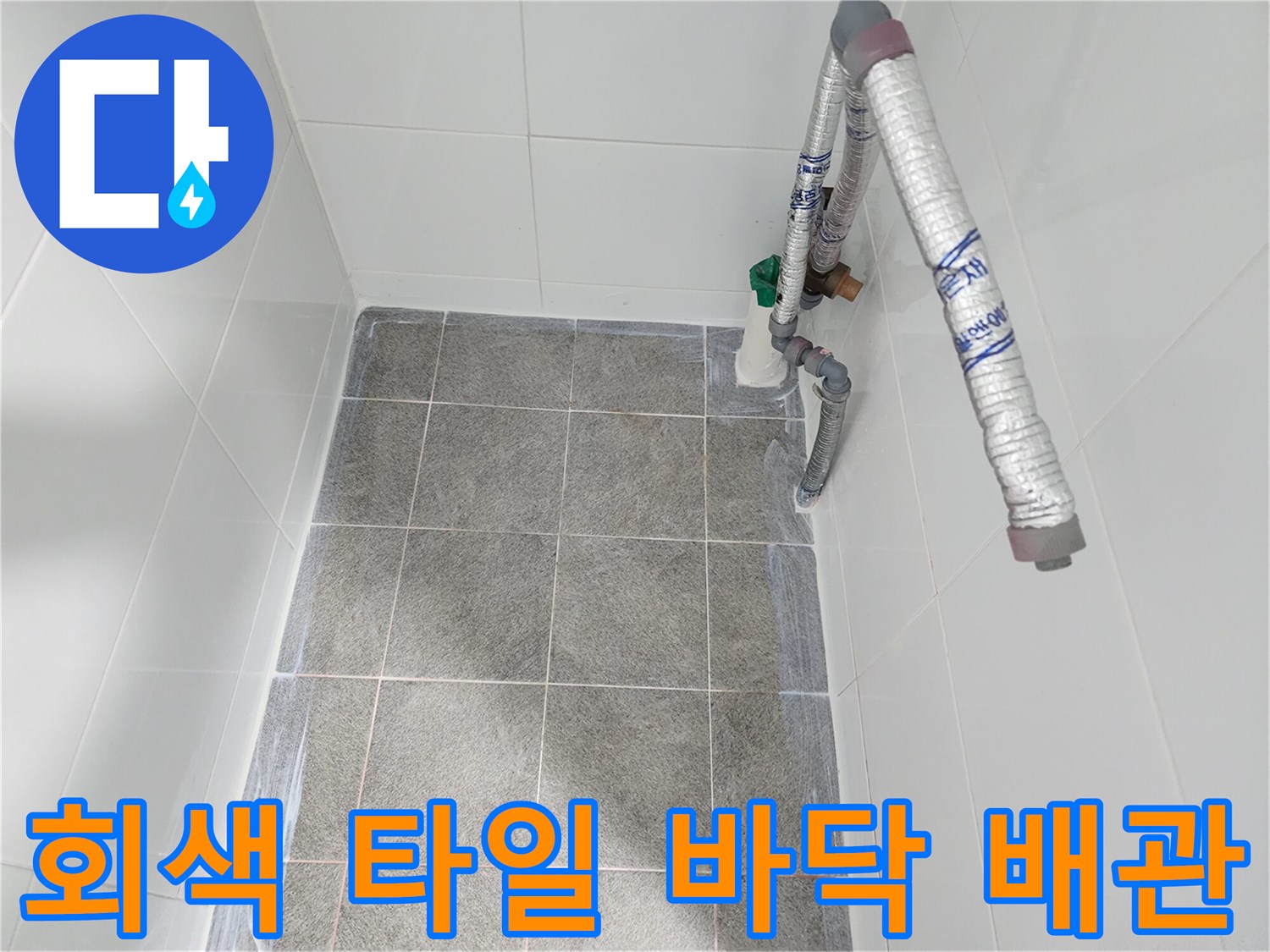 욕실 내 회색 타일과 은색 보온재가 씌워진 배관의 모습