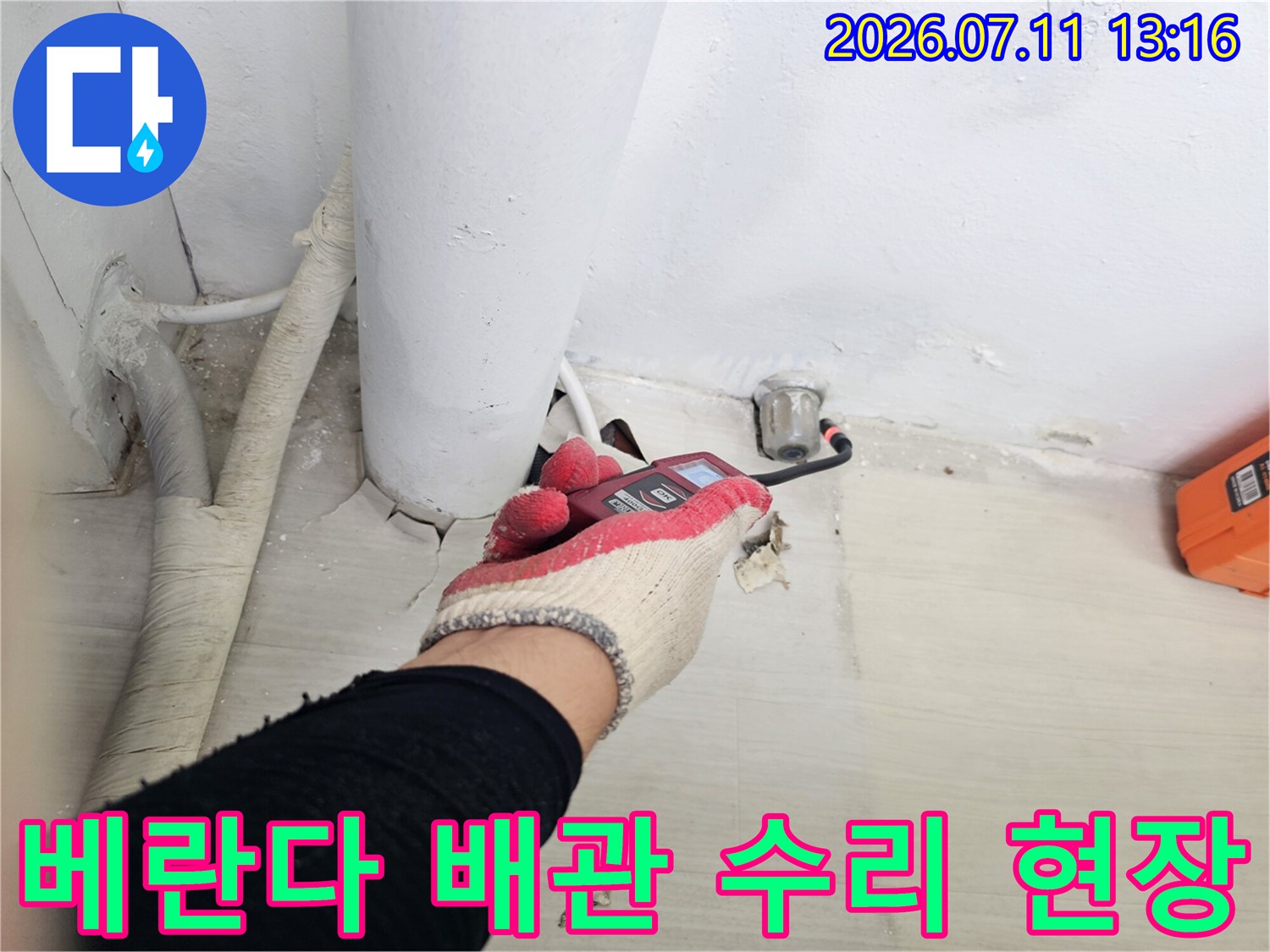 작업자가 장갑을 끼고 렌치로 베란다 바닥 관통 배관 연결부를 점검하는 모습