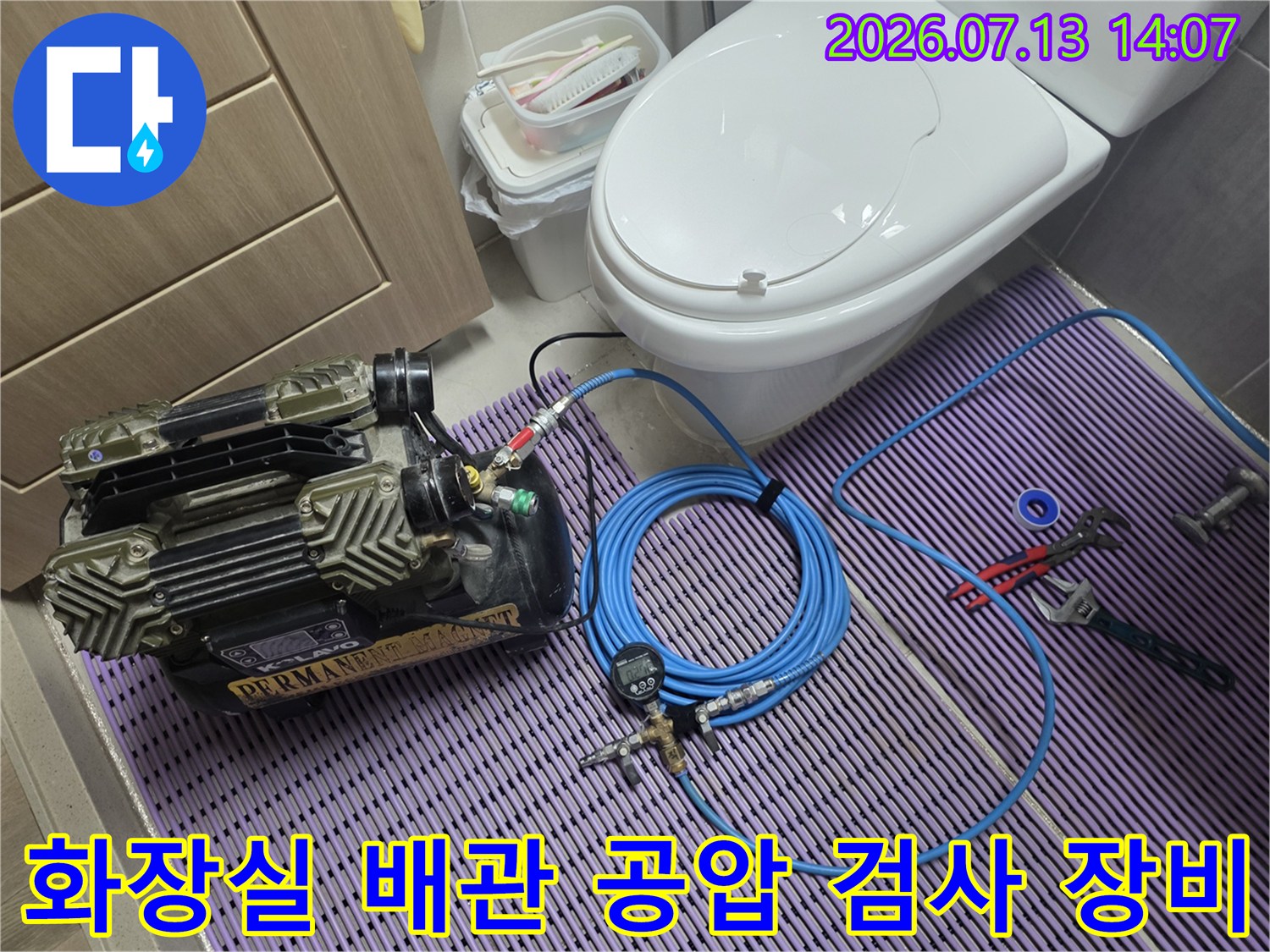 화장실 바닥에 설치된 전문 누수 탐지용 공압 검사기와 연결된 파란색 호스