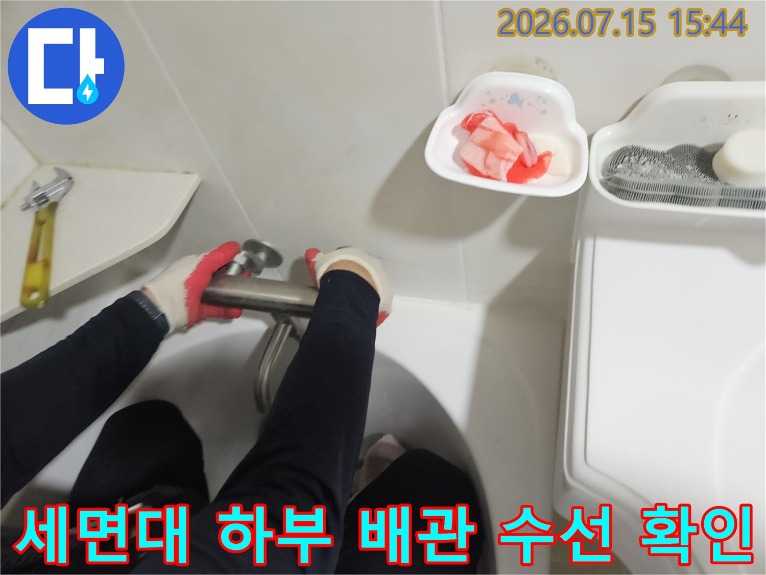 장갑을 낀 작업자가 세면대 아래쪽 파손된 배관 부분을 점검하는 장면