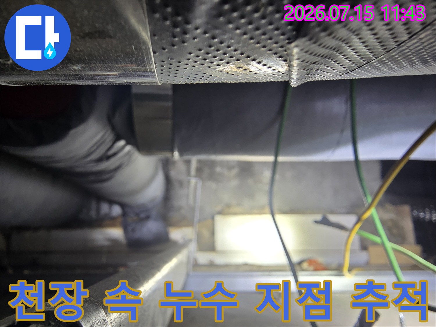 어두운 천장 내부-좁은 틈 사이에서-보온재로 마감된 두꺼운 관을 점검하는 모습