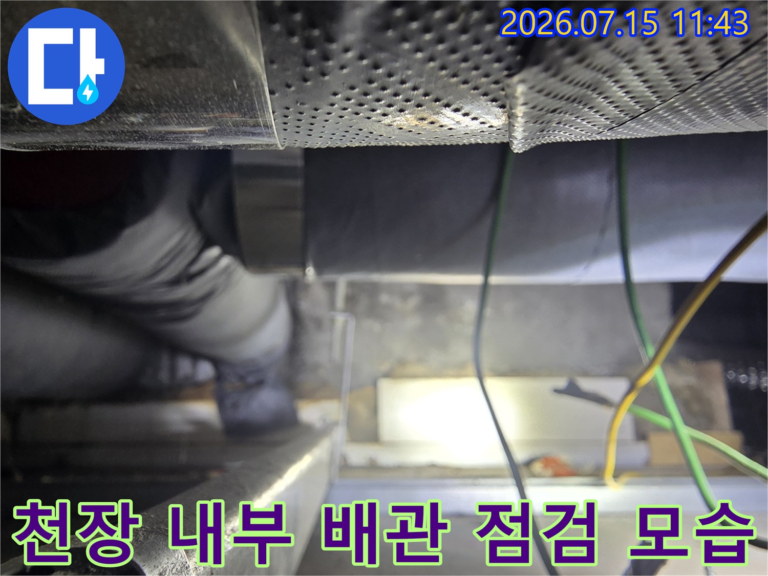 좁은 천장 공간-내부에서-배관과 전선을-점검하고 있는-작업자의-모습