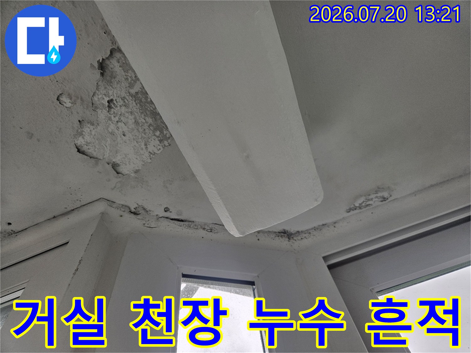 흰색 기둥 옆 거실 천장에 발생한 누수로 인한 석고보드 파손과 오염 부위
