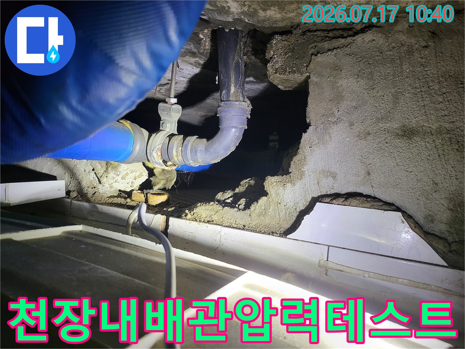 천장 점검구 내부에 노출된 배관에 압력 게이지용 호스를 연결하여 테스트하는 장면