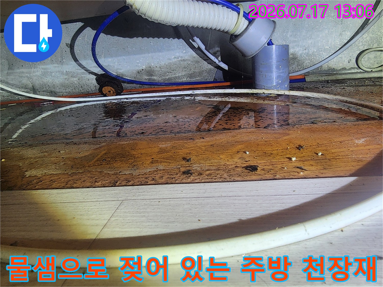 흰색 배관과 파란색 호스 주변의 목재 판넬이 누수로 인해 갈색으로 변한 모습