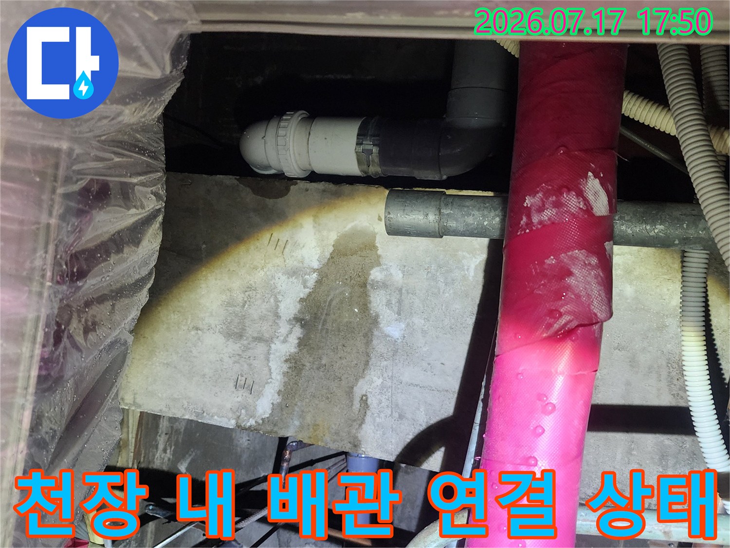 분홍색 보온재가 씌워진 파이프-아래쪽으로 이어진 회색 PVC 하수관의 모습
