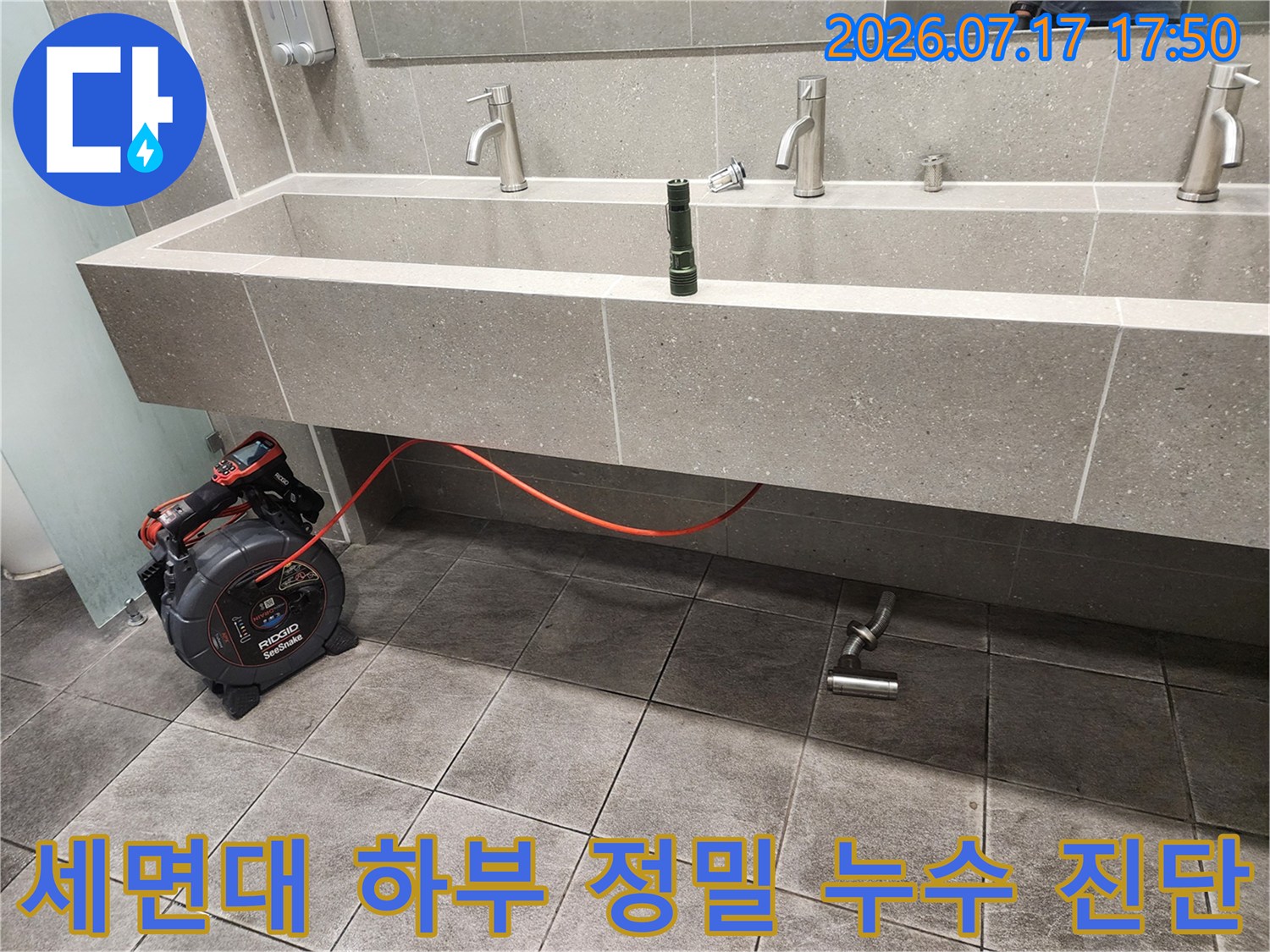 회색 타일 마감 세면대 아래에 배치된 누수 탐지 장비와 빨간 호스