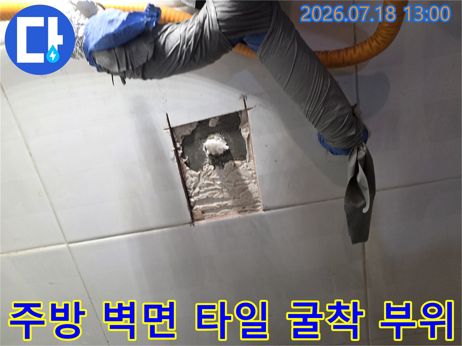 하얀색 타일 벽면에 사각형으로 굴착된 구멍과 내부의 회색 시멘트 벽체-상단에는 보온재로 감싸진 배관이 지나가는 모습
