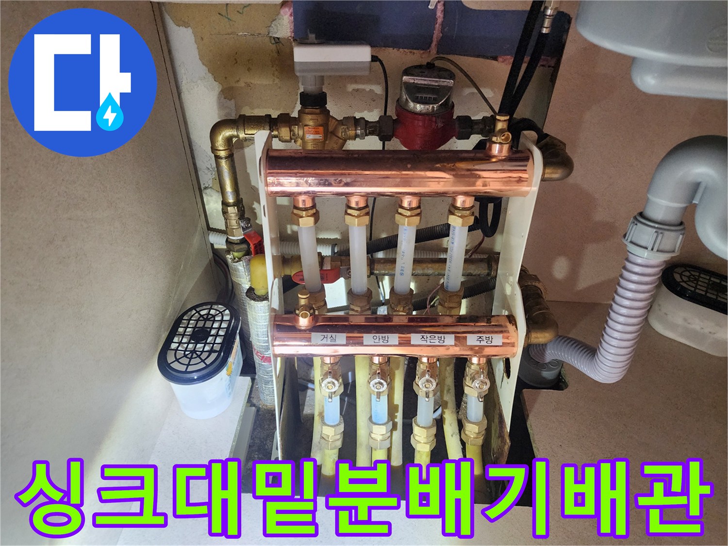 주방 하부장에 위치한 구리 소재 난방 분배기와 연결된 노란색 배관들