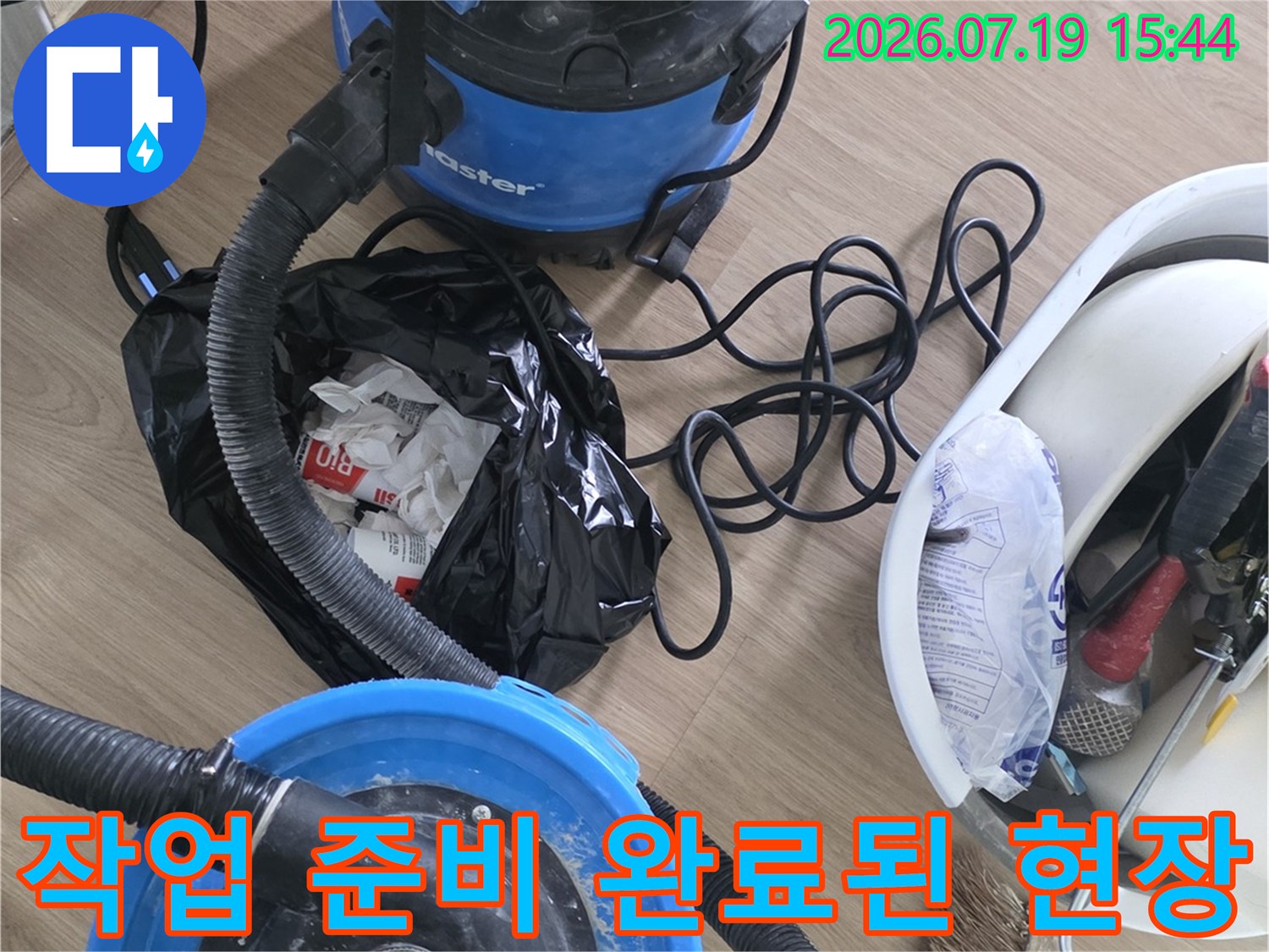 파란색 진공 청소기와 검은색 쓰레기 봉투 그리고 도구함이 놓인 모습