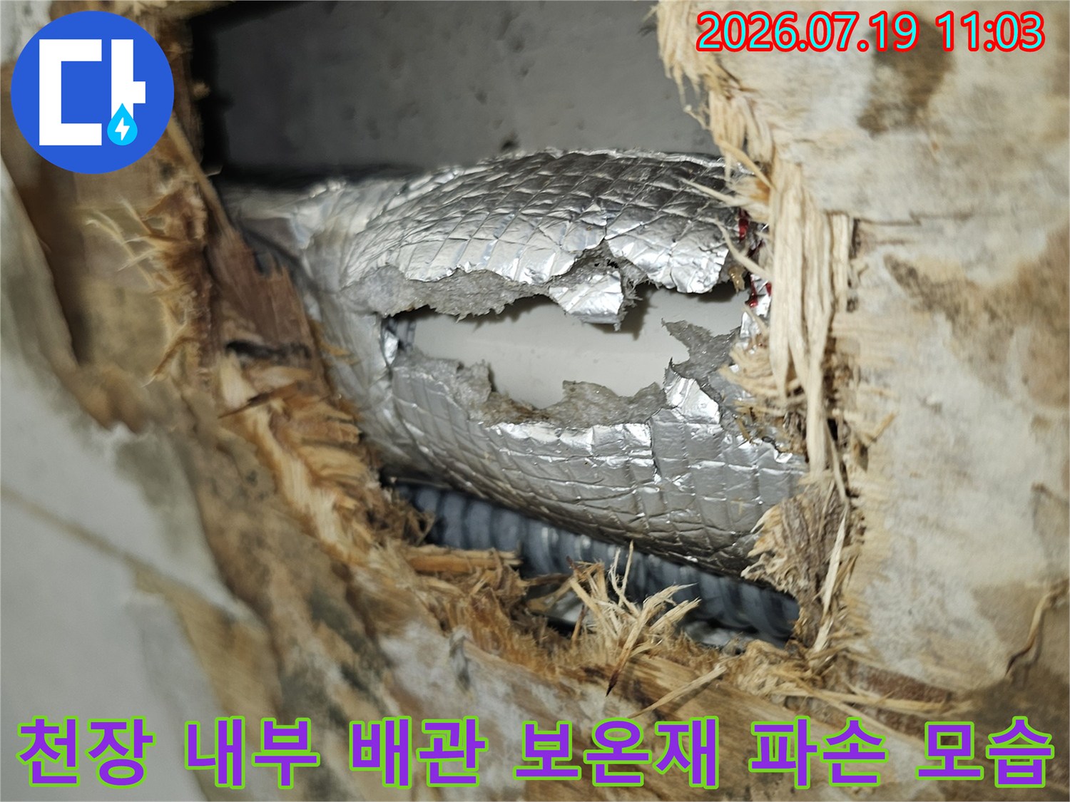 은색의 배관 보온재가 갈라지고 주변 단열재가 누수로 인해 젖어 있는 천장 내부 사진