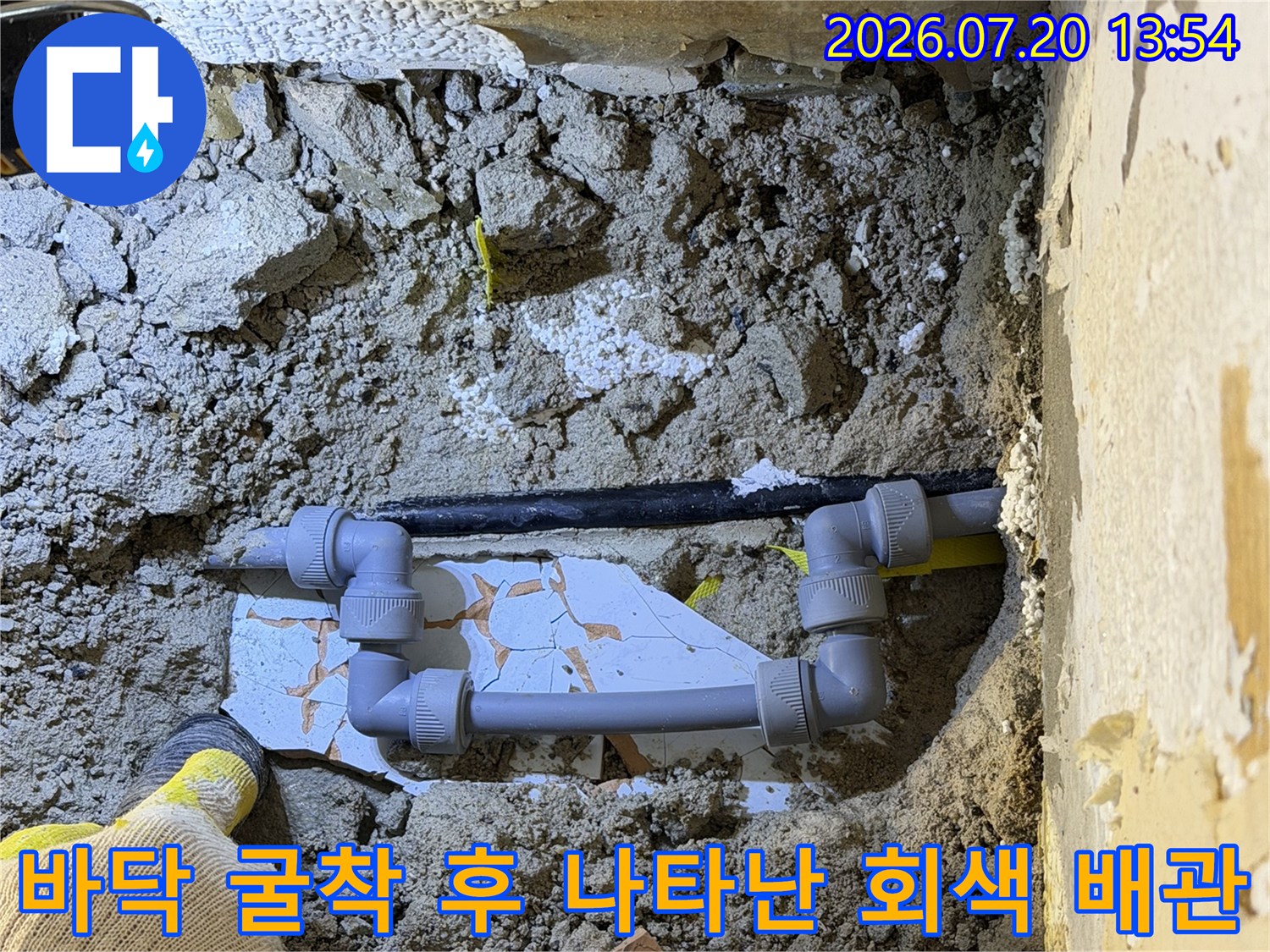 회색 플라스틱 소재의 ㄴ자 수도 배관-굴착된 바닥면과 작업자의 손이 함께 찍힌 사진