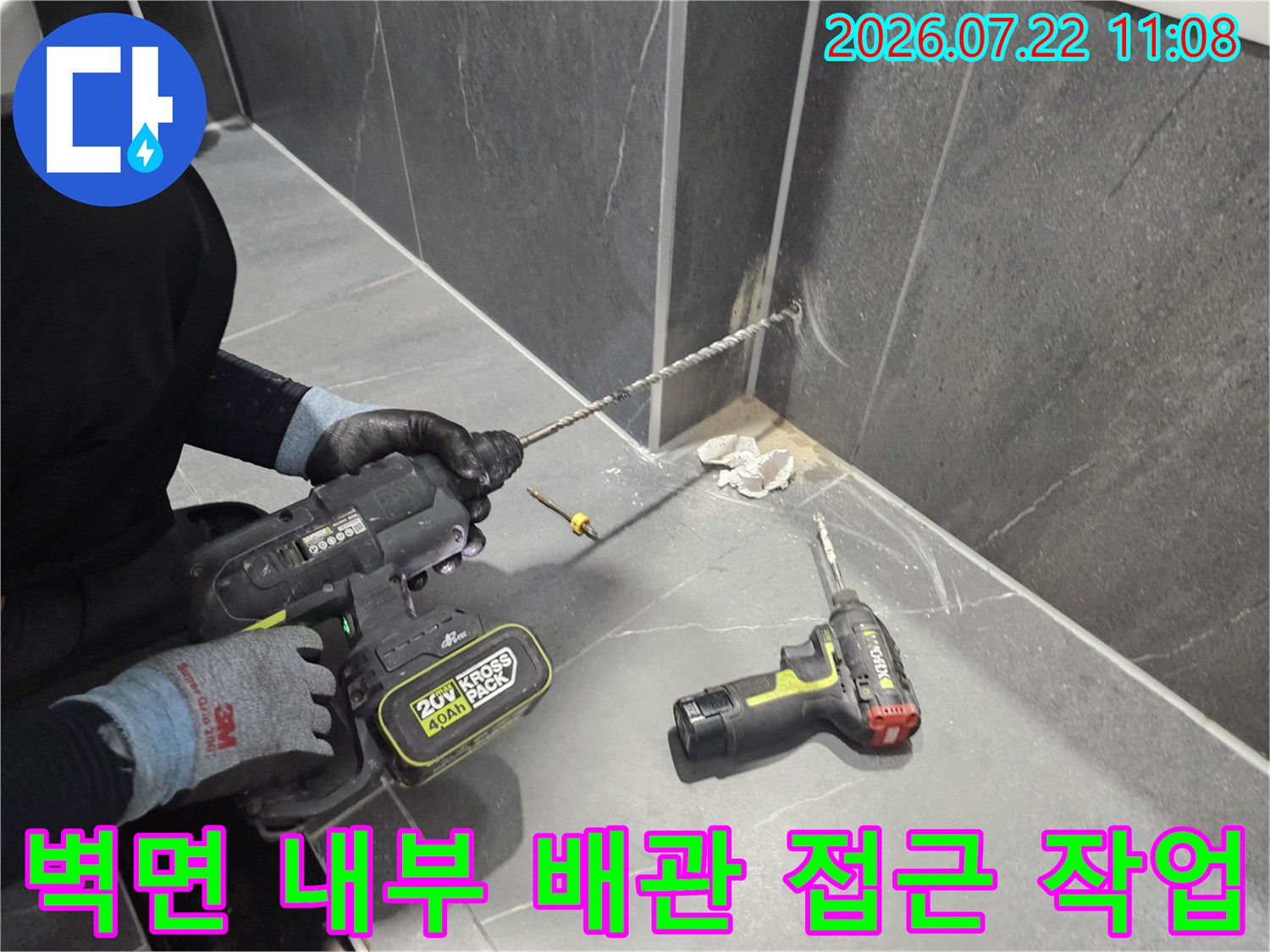 회색 대리석 타일 벽면에-전동 드릴을 사용하여 구멍을 뚫고 있는 현장 사진