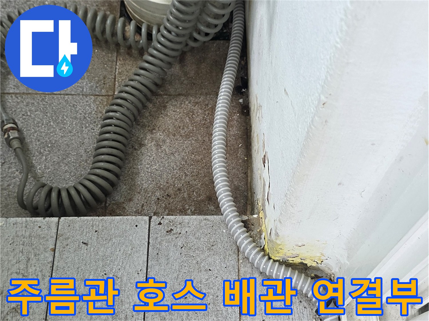 하얀색 수직 관과 회색 주름관이 만나는 지점의 근접 사진입니다.