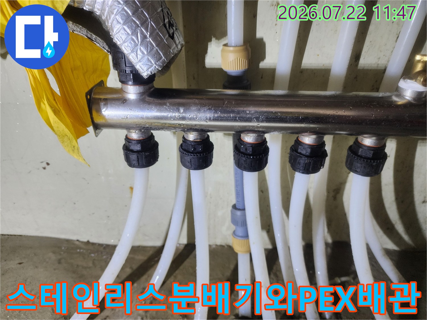 흰색 난방 배관들이 검은색 캡으로 고정되어 스테인리스 분배기 본체에 연결된 사진