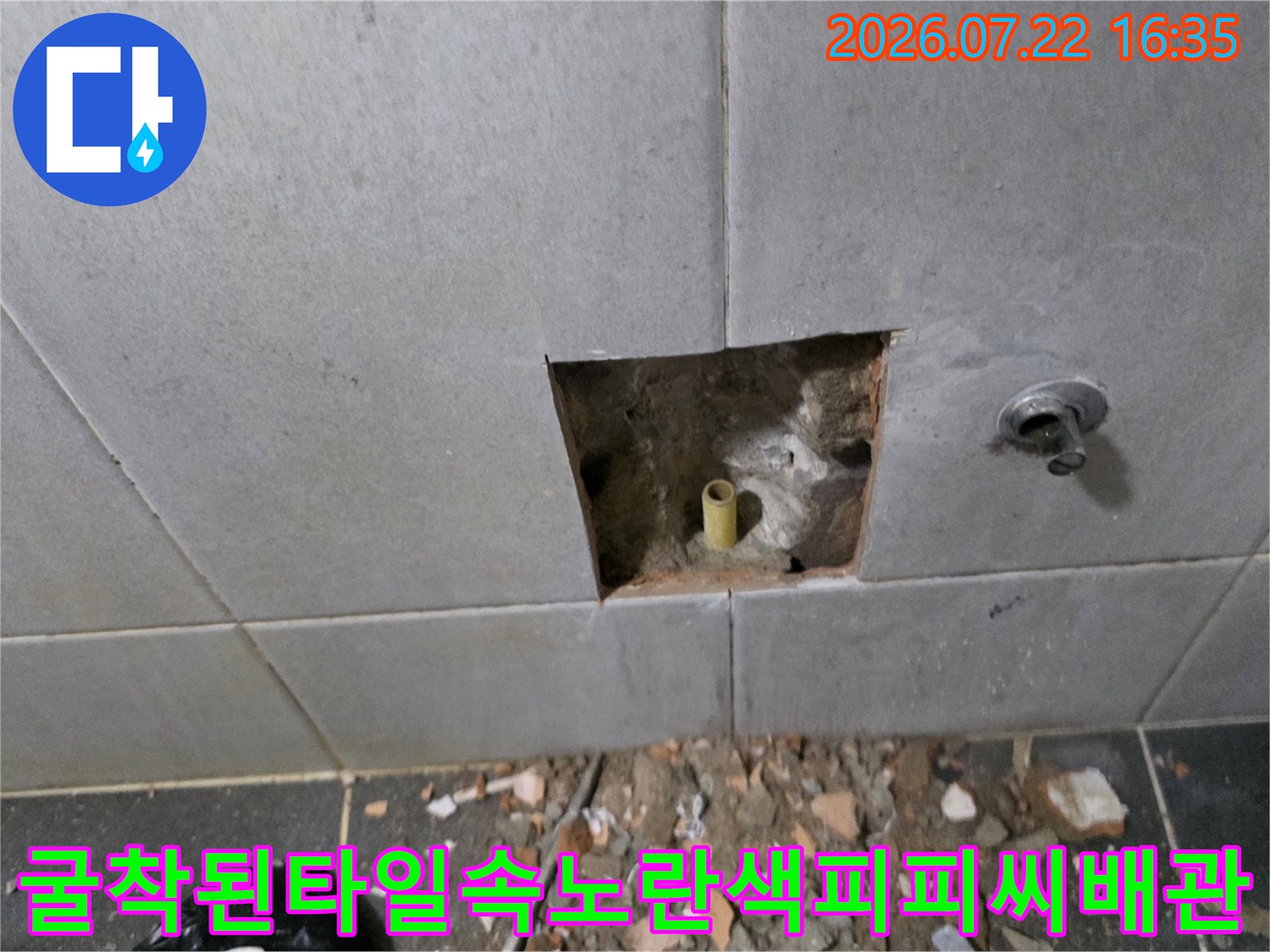 회색 타일 벽면에 사각형으로 파낸 구멍 속에 노란색 수도 배관이 노출되어 있는 모습