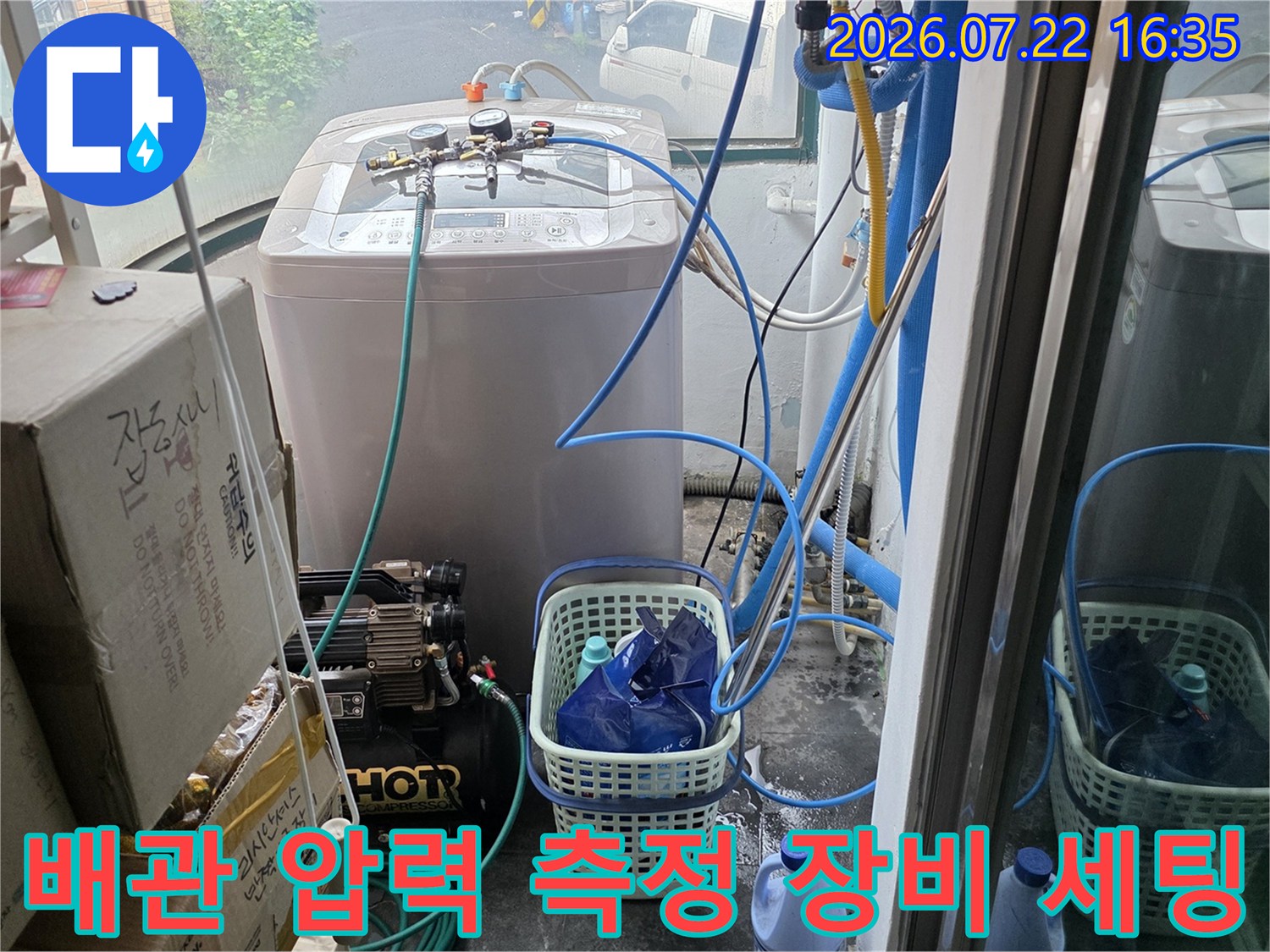 흰색 가전제품 옆에 설치된 파란색 배관 호스와 누수 탐지용 컴프레셔 장비