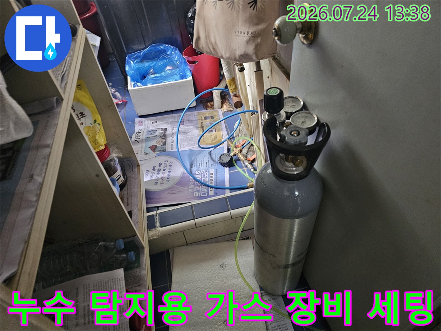 바닥에 놓인 회색 가스 탱크와 파란색 호스가 연결된 누수 탐지 전문 장비