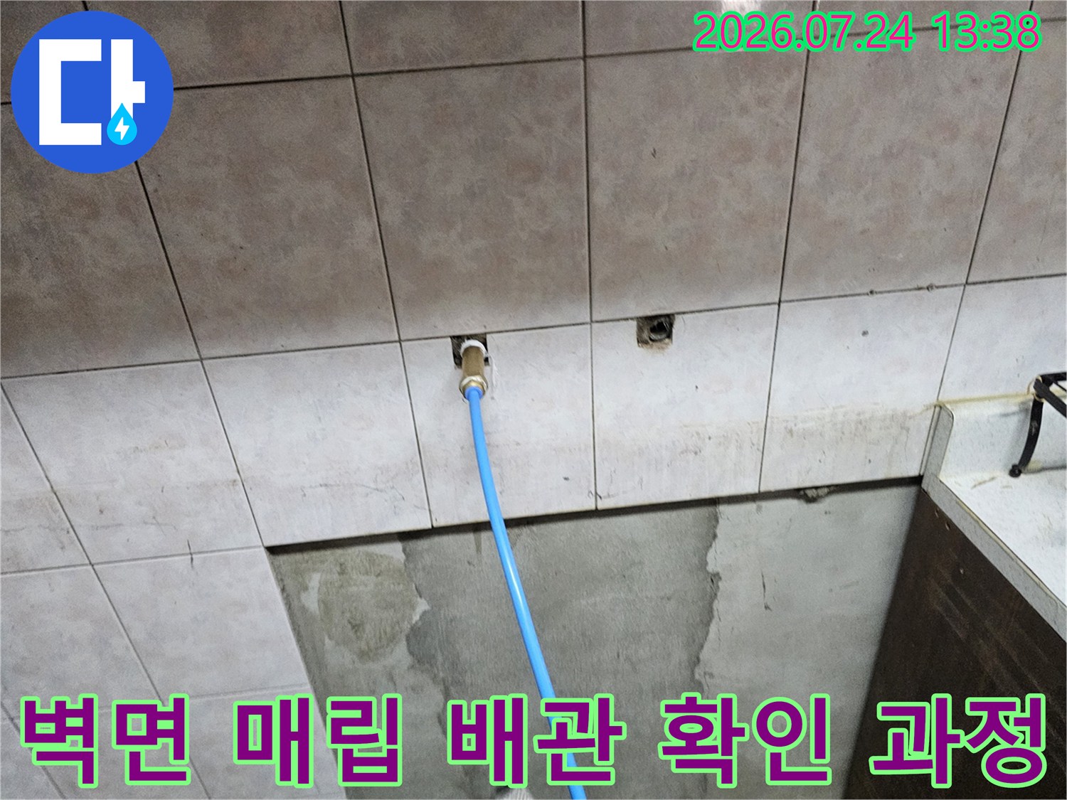 베이지색 타일 벽면에 파란색 누수 점검용 배관이 연결된 모습