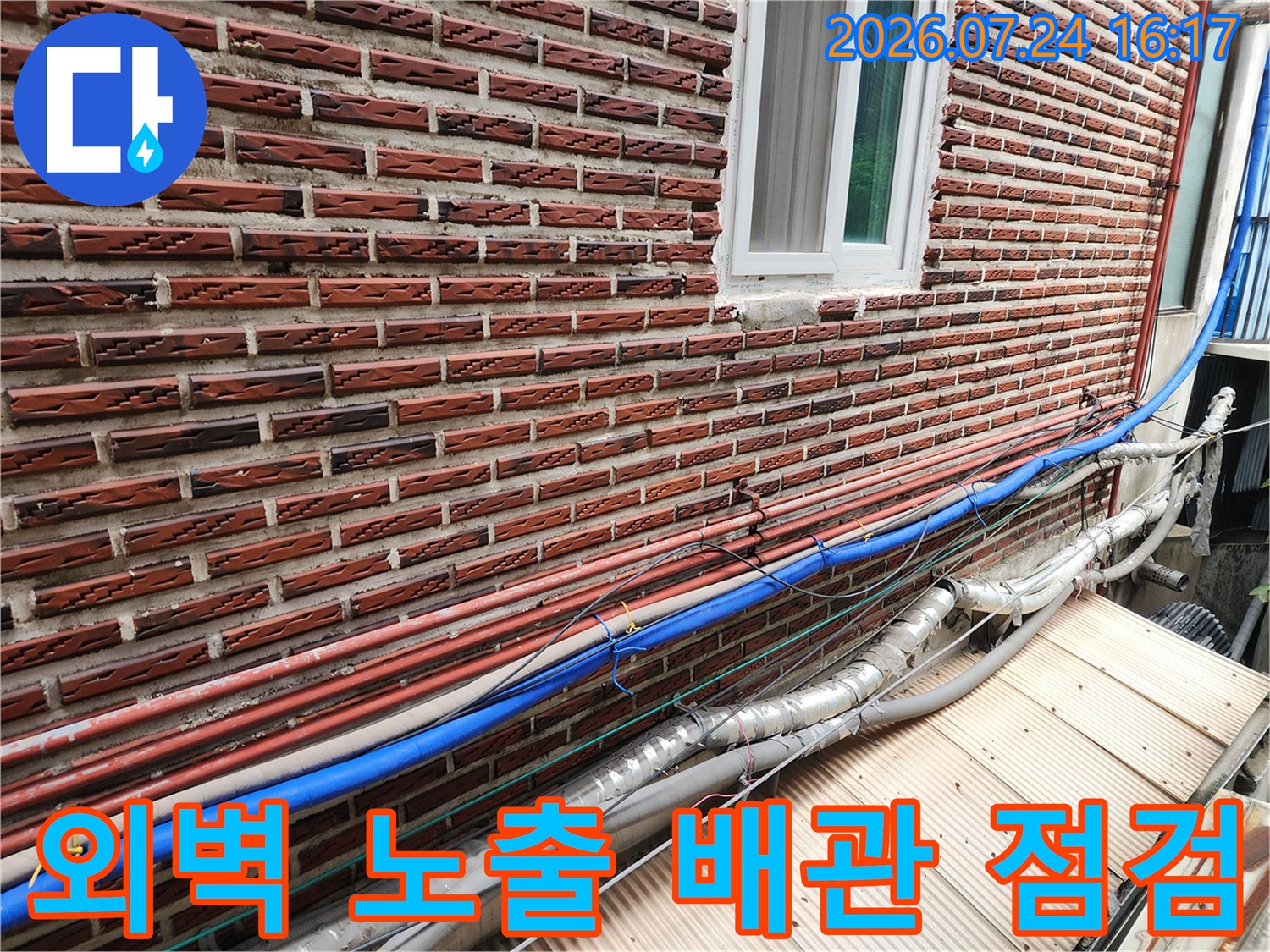 붉은 벽돌 외벽을 따라 배치된 파란색과 은색의 복합적인 수도 배관 시설
