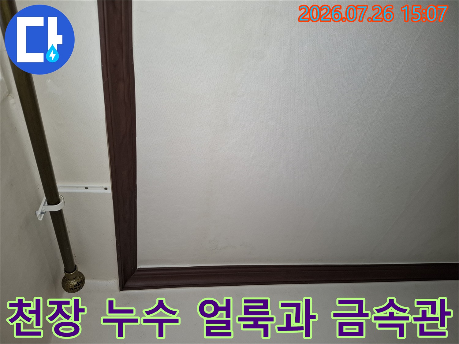 흰색 천장에 번진 노란 누수 자국-왼쪽에 설치된 금속 배관 파이프