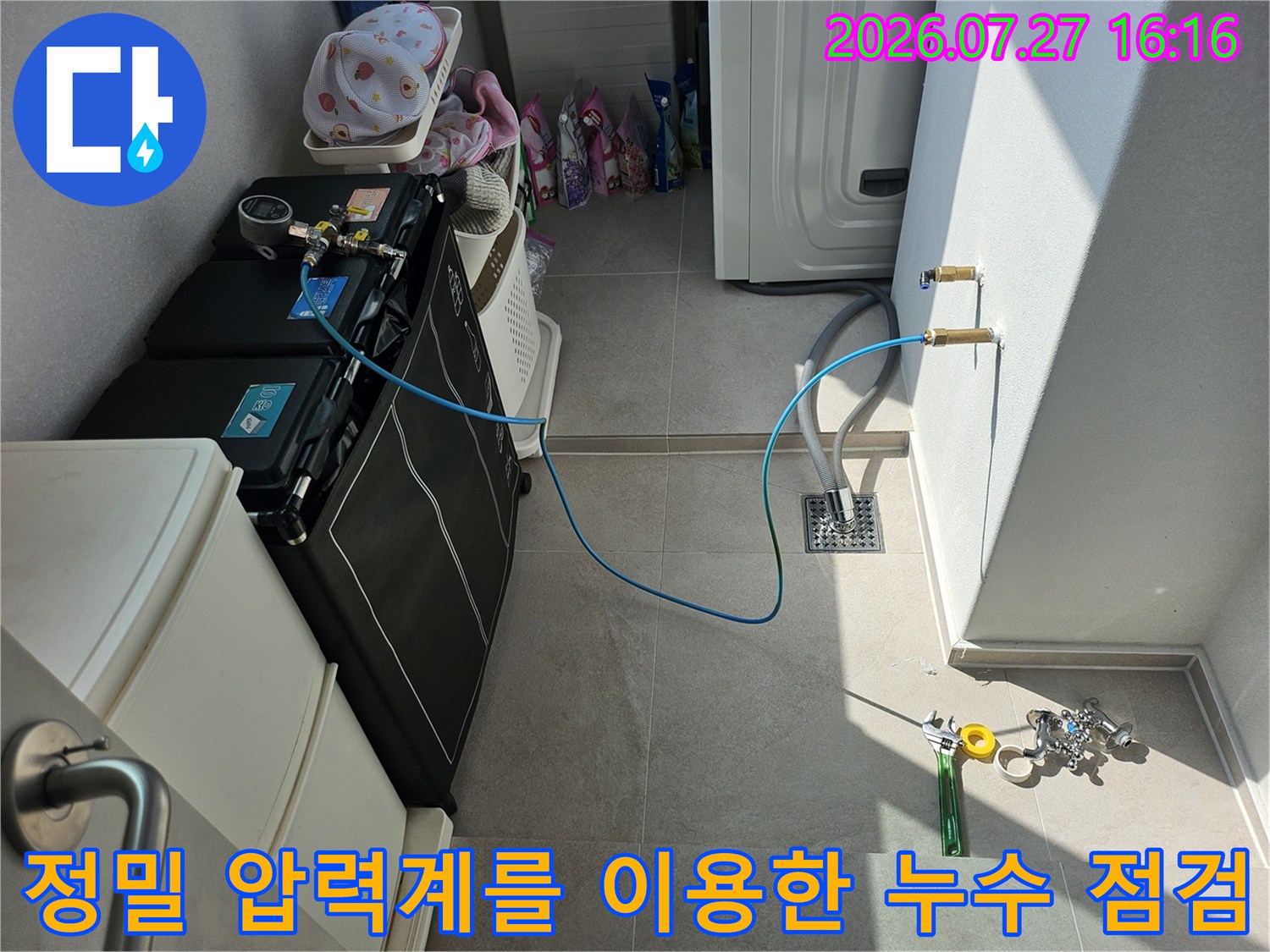 벽면의 급수 밸브에 파란색 호스를 연결하고 바닥에 압력 측정기를 배치한 작업 상황