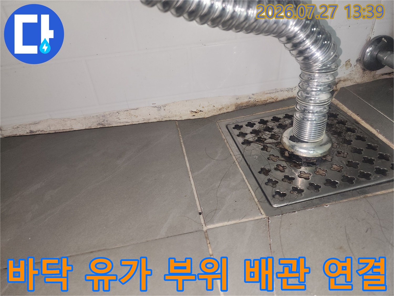회색 타일 바닥의 금속제 하수구 덮개와 위로 솟아있는 주름관 배관 사진