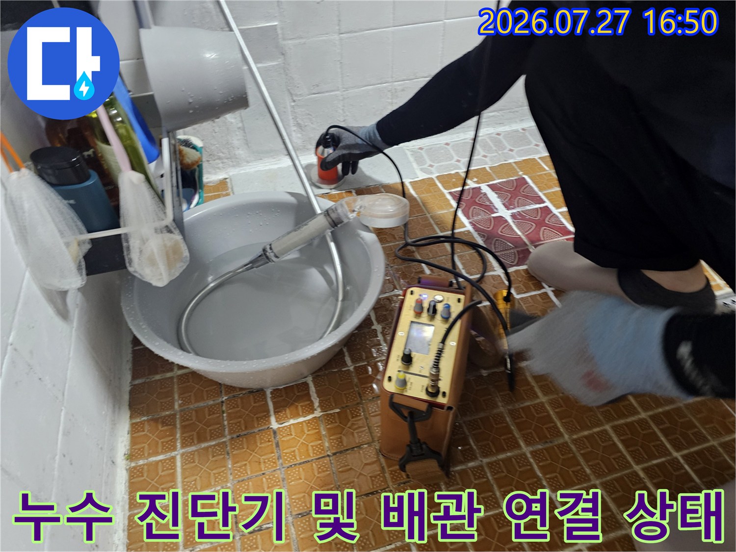 흰색 세면대 옆 바닥에 설치된 누수 탐지 장비와 측정용 호스-장치