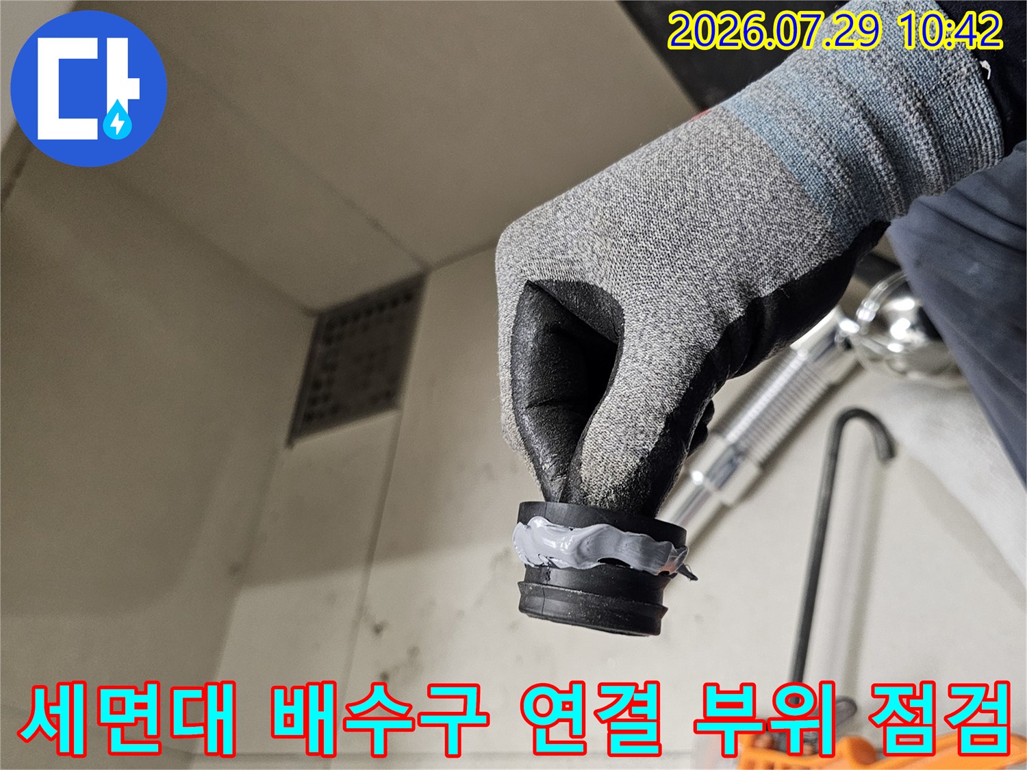 작업자가 장갑을 끼고 세면대 아래쪽의 배수관 연결 부위를 확인하는 모습