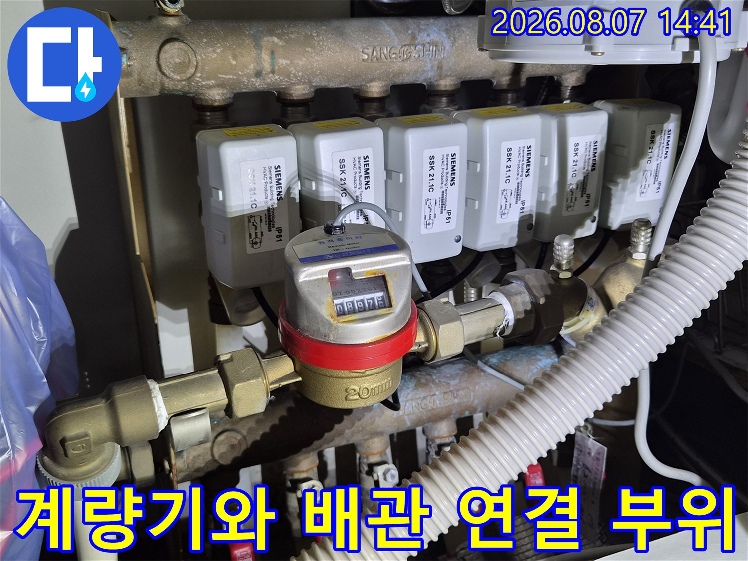 금속 재질의 수도 계량기와 상단의 전기 제어 장치가 설치된 모습입니다.